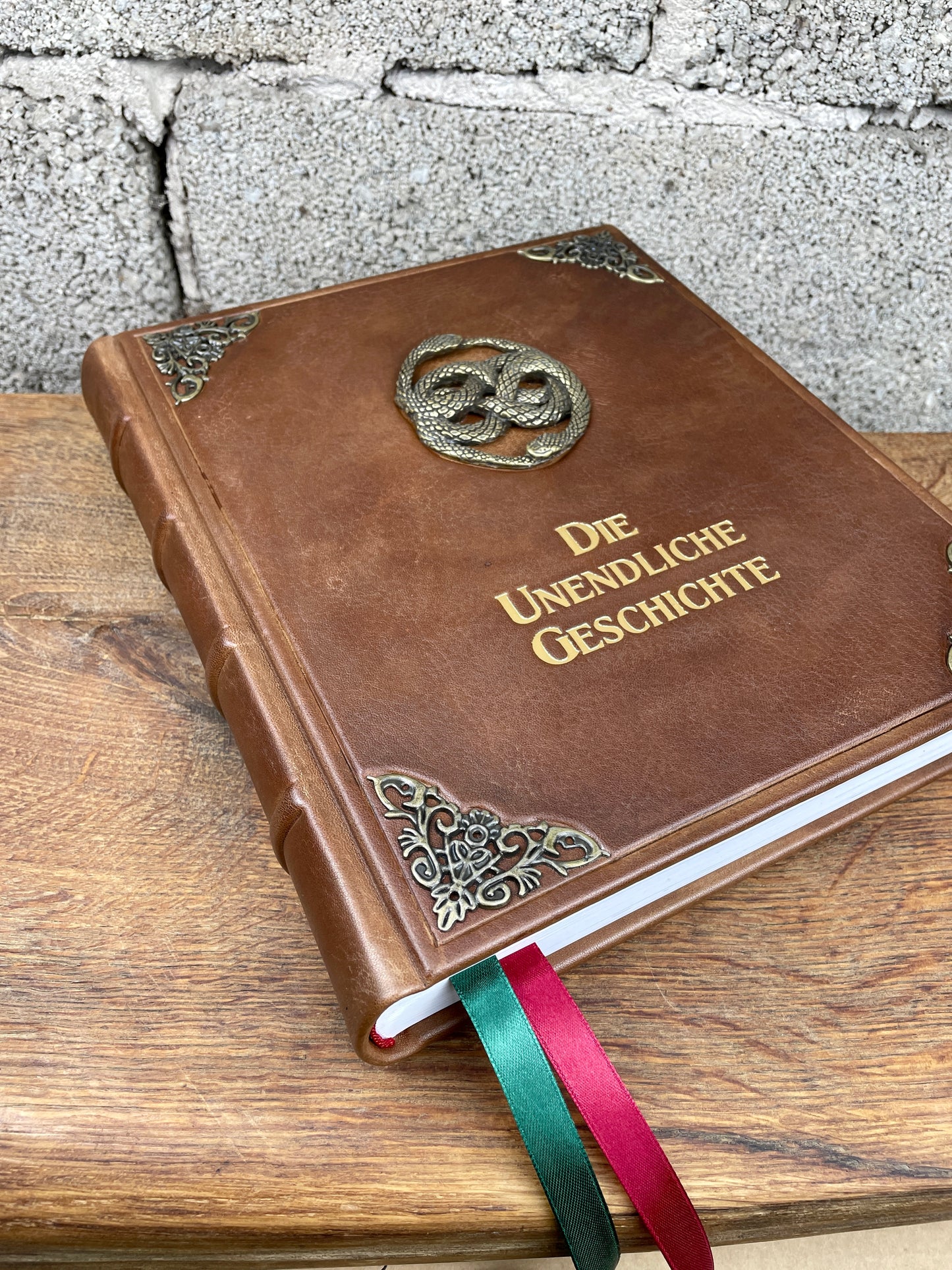 Schrägansicht der Lederausgabe der Unendlichen Geschichte mit verzierten Zierecken und goldener Titelprägung auf der Vorderseite, inspiriert vom Buch im Film.