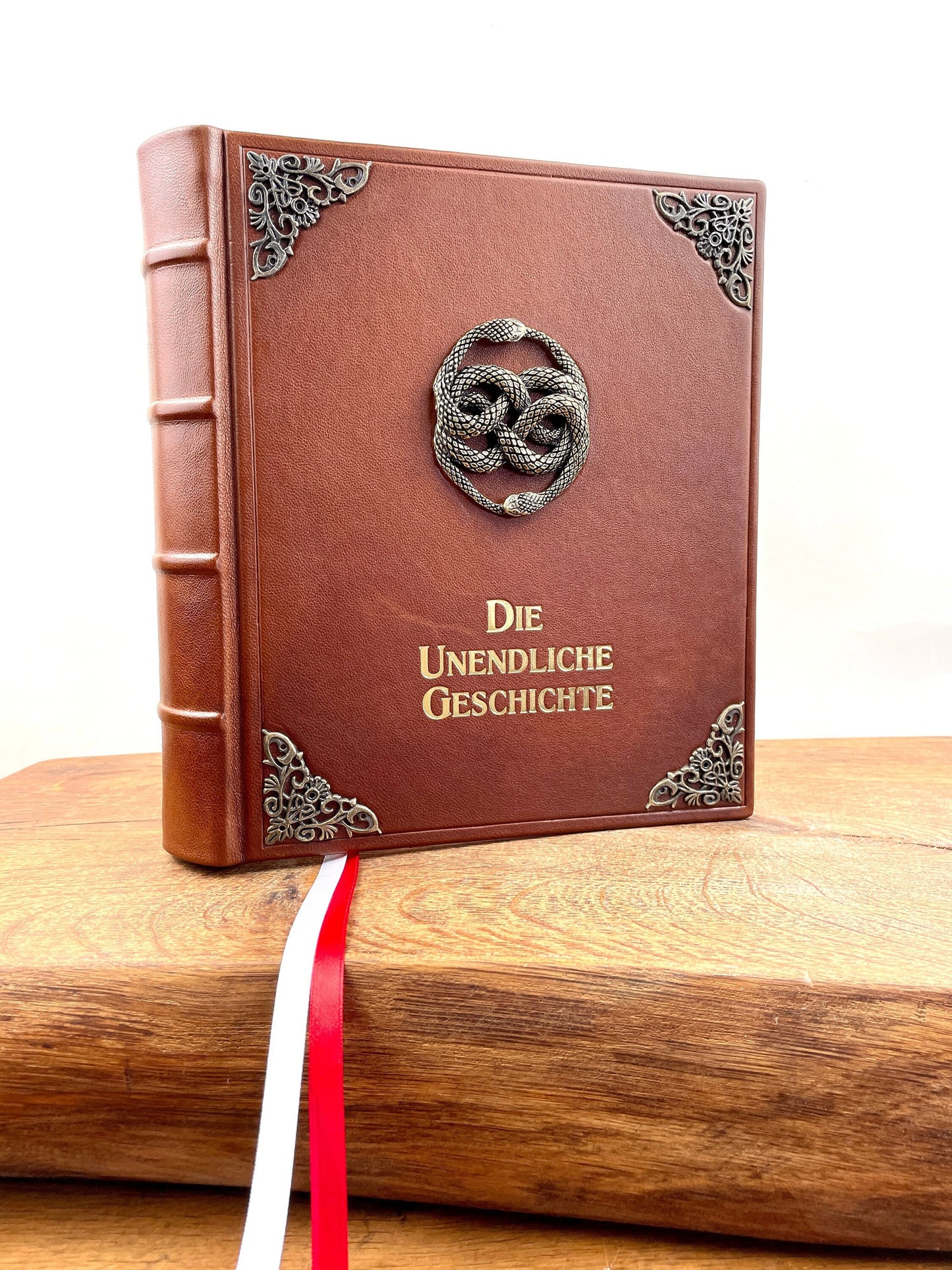 Lederausgabe der Unendlichen Geschichte in braunem Leder mit Zierecken, inspiriert vom Buch im Film. Vorderansicht mit detailreichem, großen AURYN-Emblem in der Mitte und goldener Titelprägung.